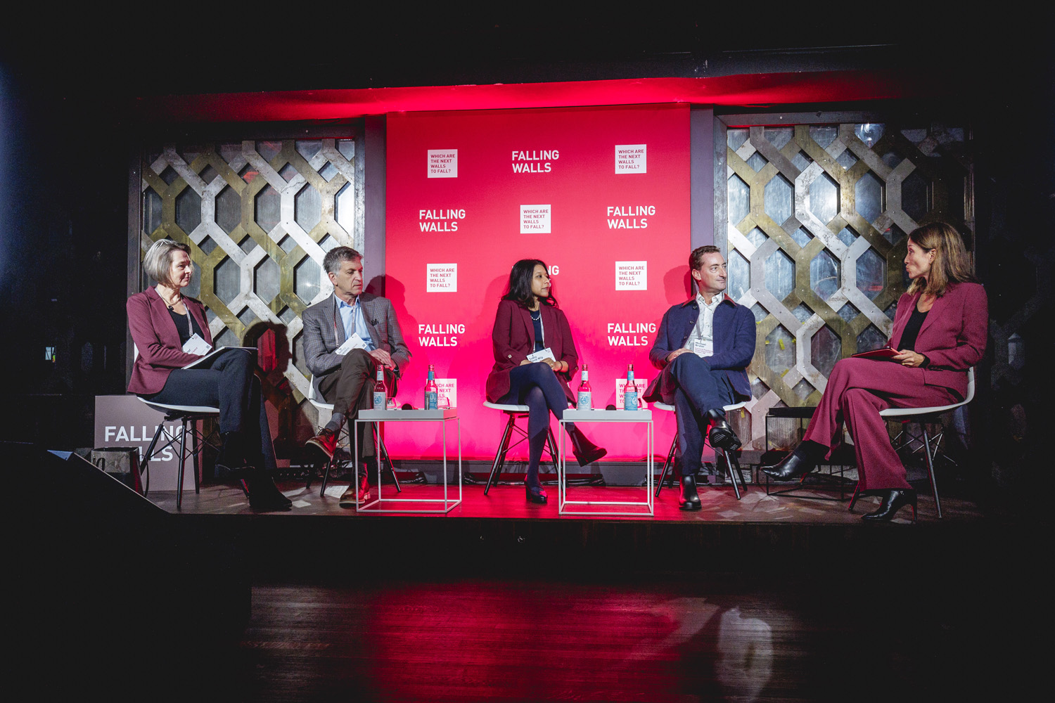 A panel of people sitting on a stage against a grey and pink background