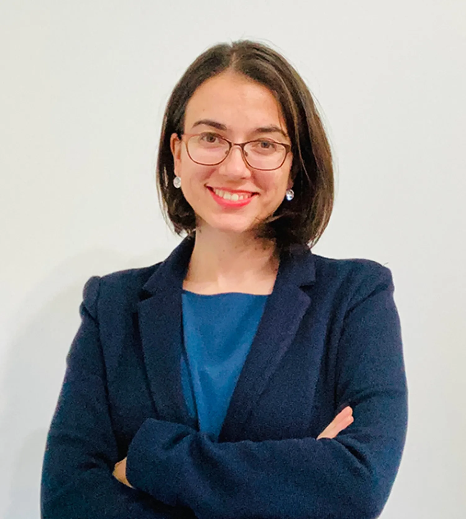 Image of a woman wearing glasses, a dark blue jacket and blue top smiling at camera