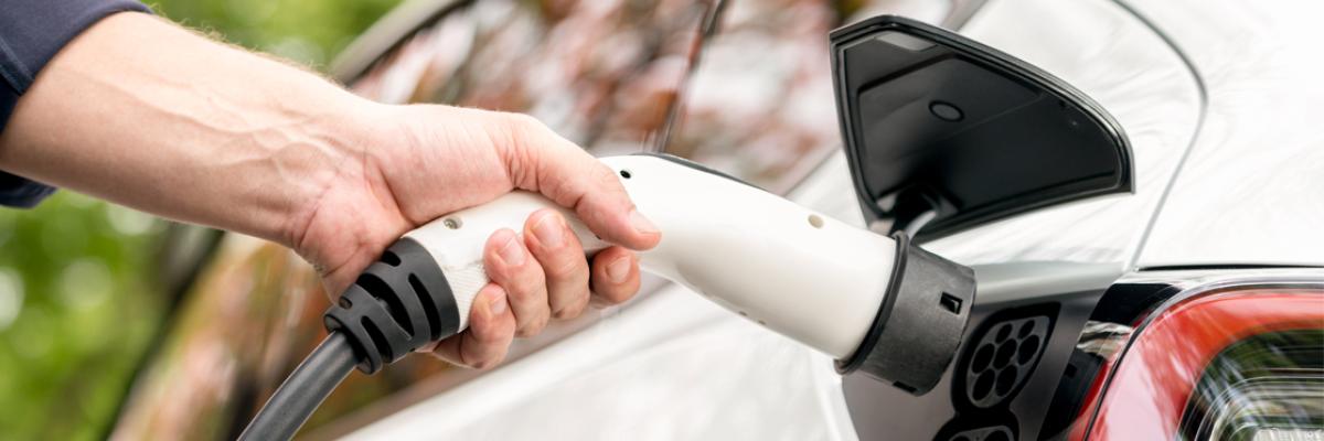 a man holding a charge cable to a car