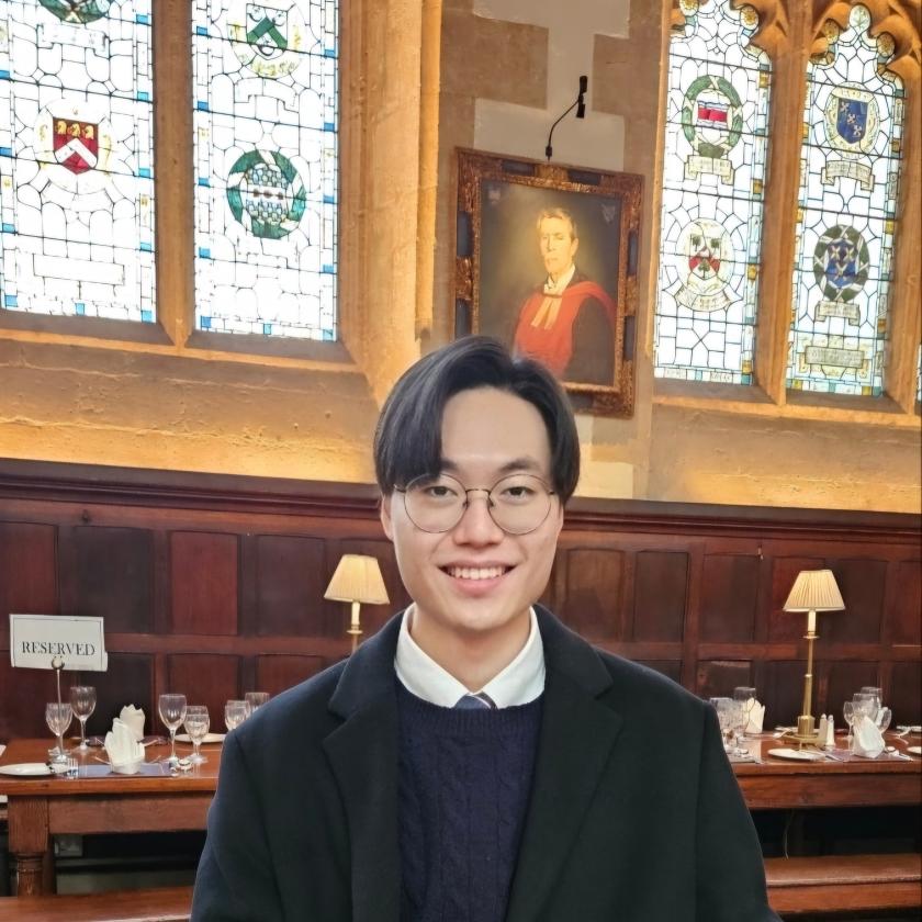 Image of a man wearing glasses and a dark blazer smiling at camera