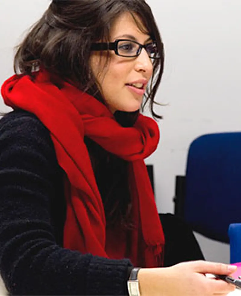 An image of a woman wearing glasses sat sideways working at a desk